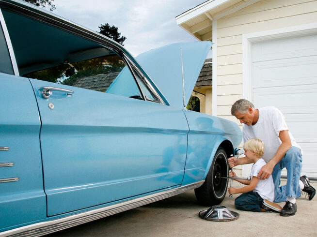 Young boy learning how to change tire with grandpa on classic car