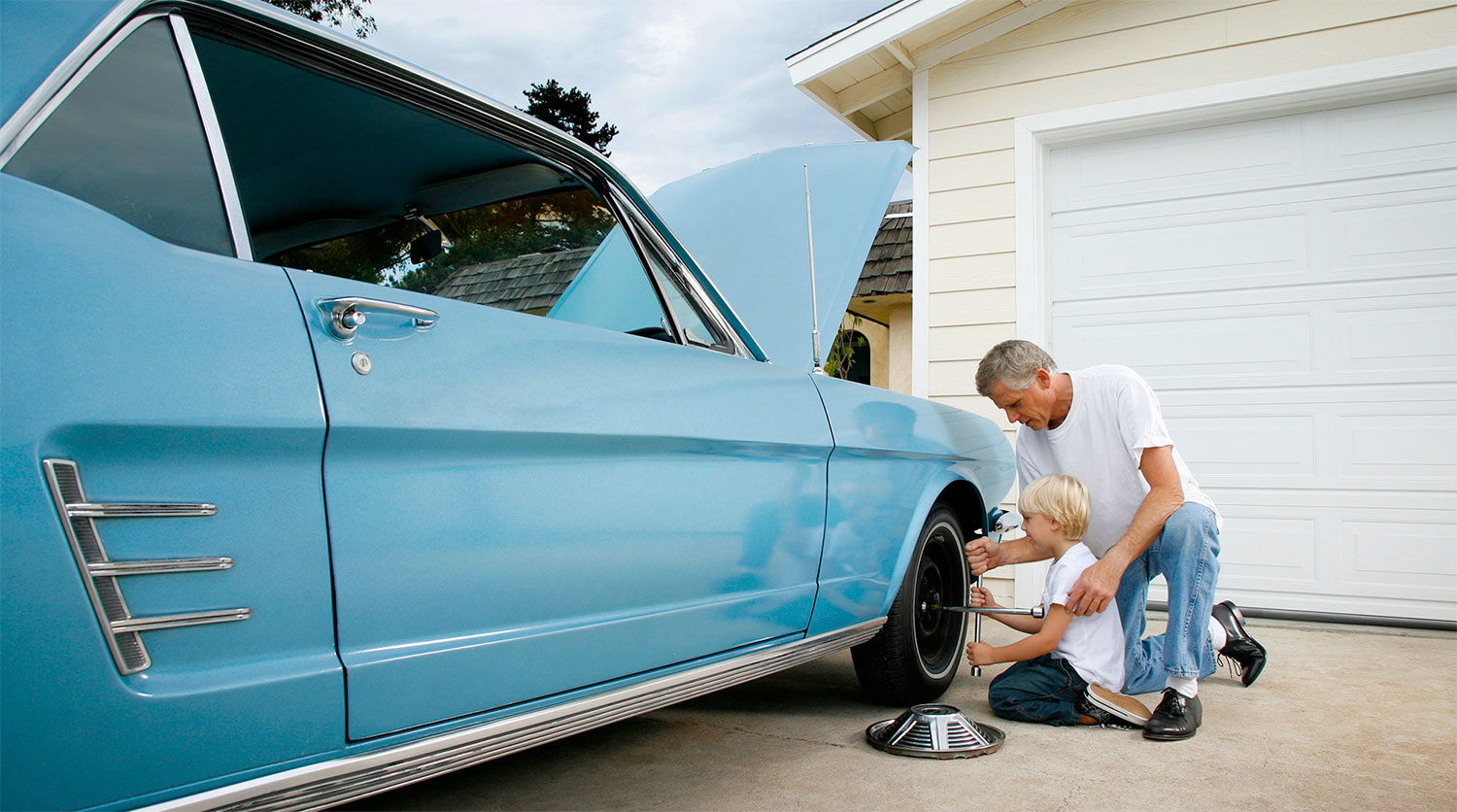 Young boy learning how to change tire with grandpa on classic car